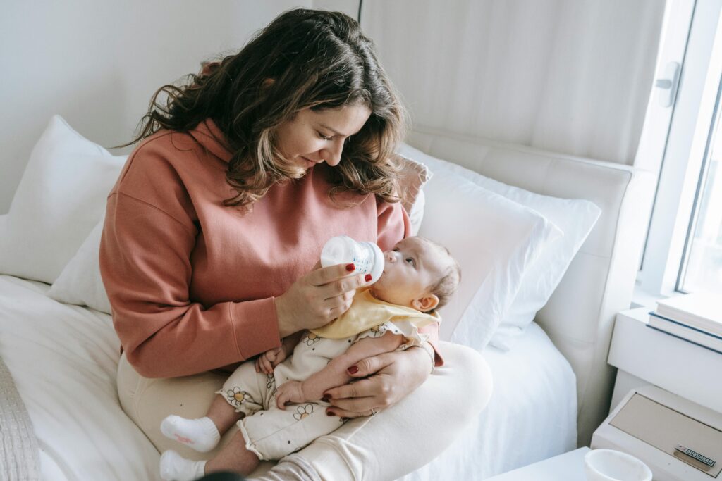 A mother lovingly feeds her newborn baby with a bottle in a cozy bedroom.